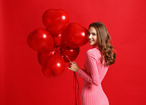 young beautiful emotional girl in pink dress with red ballons on red background