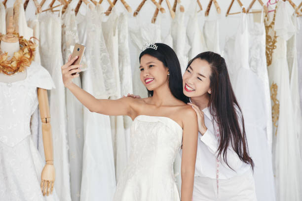 braut und schneiderin stehend und selfie bild zusammen während hochzeitskleid trial in boutique-zimmer - veil bride lace married stock-fotos und bilder