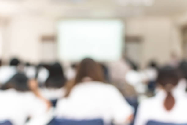 istock School classroom blurred background of college or university students back view sitting in class in seating rows studying learning course in lecture room with white projector screen in front 1076327238