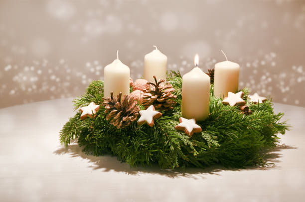 First Advent - decorated Advent wreath from fir and evergreen branches with white burning candles, tradition in the time before Christmas, warm background with festive bokeh and copy space stock photo