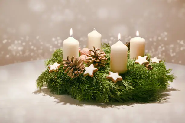 Third Advent - decorated Advent wreath from fir and evergreen branches with white burning candles, tradition in the time before Christmas, warm background with festive bokeh and copy space, selected focus