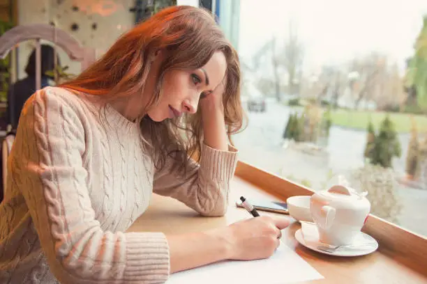 Photo of Sad young woman writing letter with broken heart