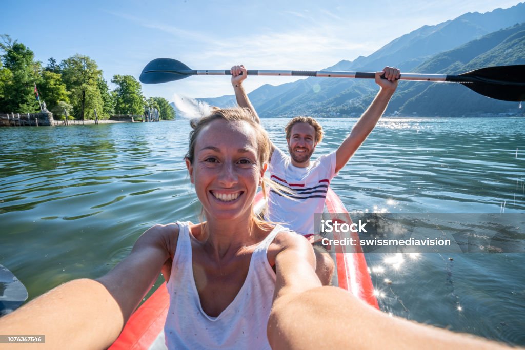 Young couple taking selfie portrait in red canoe on mountain lake Young couple canoeing take selfie on beautiful mountain lake in Switzerland. 
Inflatable red canoe on water with mountain scenery
People travel outdoor activity concept Selfie Stock Photo