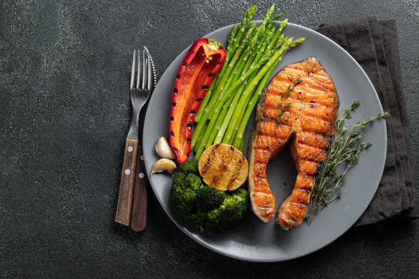 tasty and healthy salmon steak with asparagus, broccoli and red pepper on a gray plate. diet food on a dark background with copy space. top view. flat lay - fish plate dishware dinner imagens e fotografias de stock