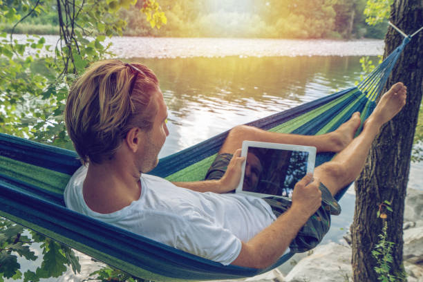 istock One male on hammock by the river using digital tablet- People travel Summer vacations technology concept 1076370766