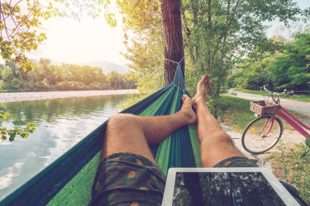 istock Personal perspective of man lying on hammock by the river using digital tablet in Summer- People travel vacations technology on the go concept 1076375970