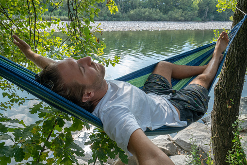 Joyful young man on hammock relaxing by the river in Summer- People travel vacations nature concept