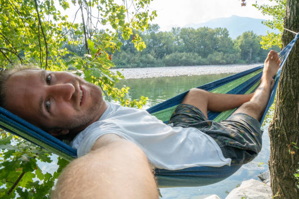 istock Young man taking selfie on hammock relaxing by the river in Summer 1076383982