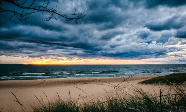 Beautiful sandy beach under dark skies and sunset horizon. Dramatic storm clouds converge over Lake Michigan at Hoffmaster State Park in the US state of Michigan for an imposing weather scene on this stormy night. High energy seascape background with copy space.