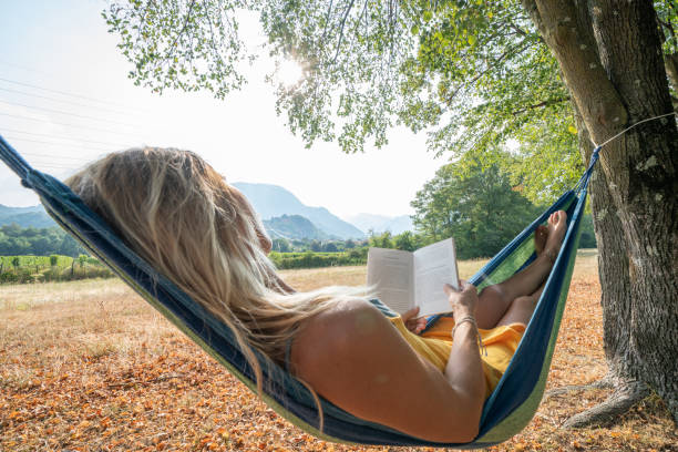 istock Young woman relaxing on hammock in nature at sunset reading book 1076458674