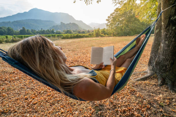 istock Young woman relaxing on hammock in nature at sunset reading book 1076459096