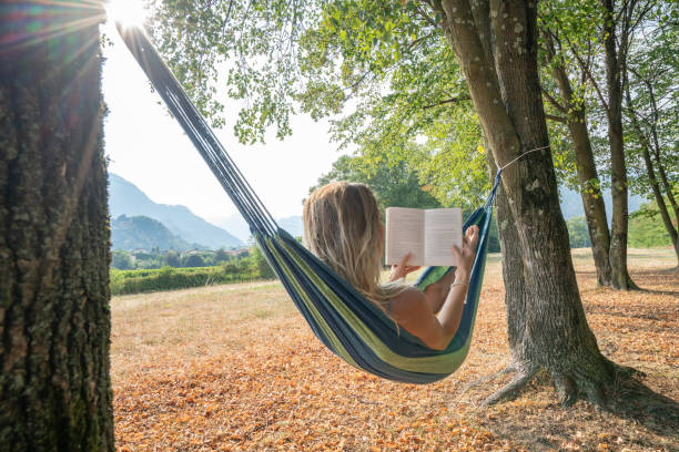 istock Young woman relaxing on hammock in nature at sunset reading book 1076465880