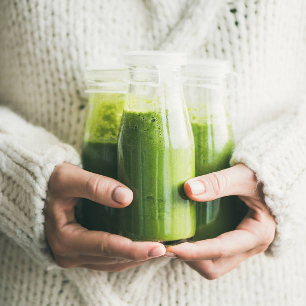 istock Green smoothie or juice in bottles in hands, square crop 1076485910