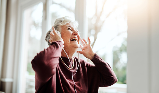 Shot of happy senior woman listening to music with headphones at a retirement home