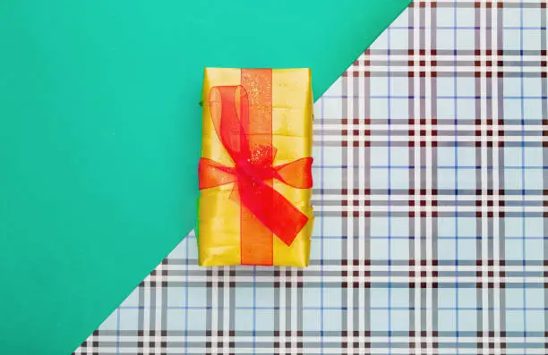 Yellow gift box with red bow on checkered and green background. Top view. Copy space. Holidays concept
