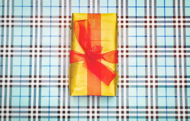 Yellow gift box with red bow on checkered background. Top view. Holidays concept