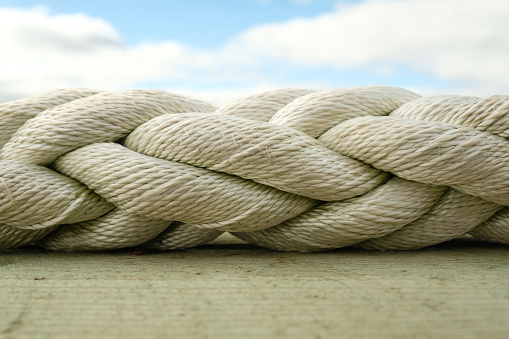 White braided rope laying horizontally between a blue sky and wood board