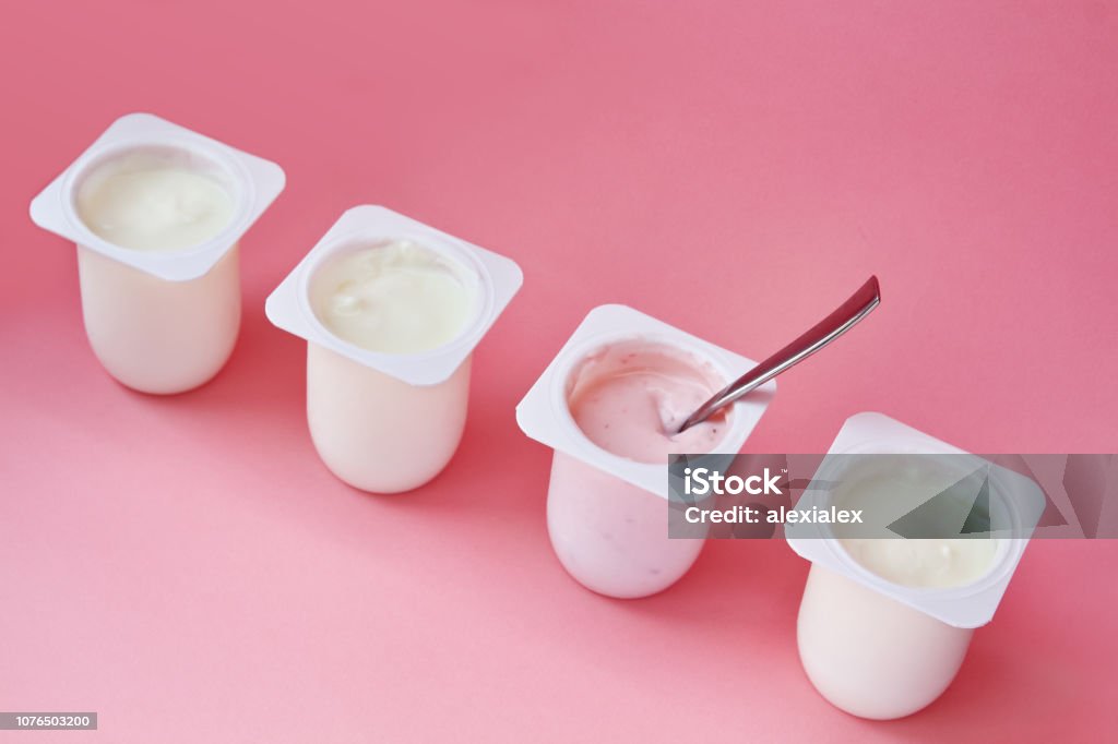Cuatro yogures en vasos de plástico blanco sobre fondo rosa en estilo minimalista. - Foto de stock de Yogur libre de derechos