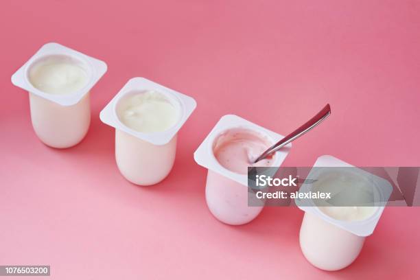 Cuatro Yogures En Vasos De Plástico Blanco Sobre Fondo Rosa En Estilo Minimalista Foto de stock y más banco de imágenes de Yogur