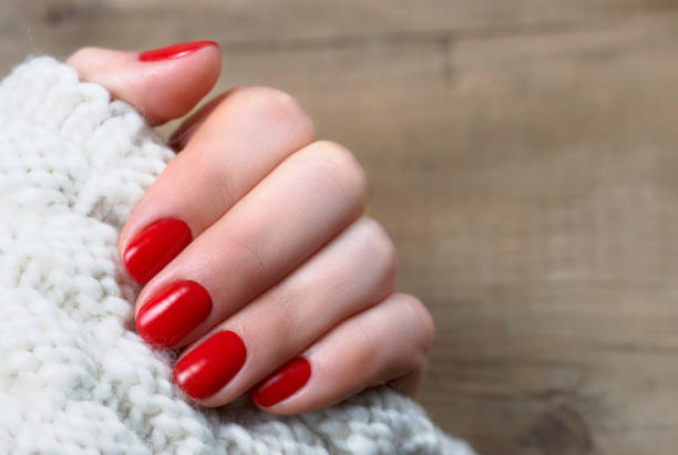 istock Female hand with red manicure on a white knitted background with copy space, top view 1076510944