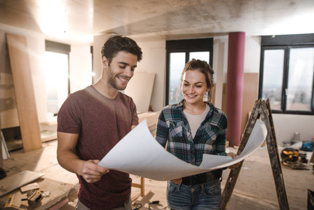 istock Young happy couple examining blueprints while being on construction site in their apartment. 1076511590