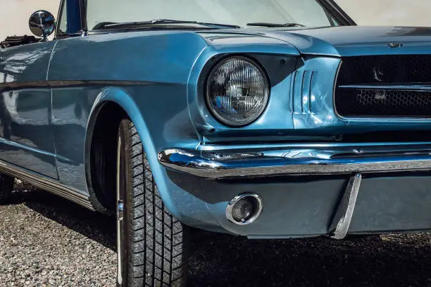 Partial close up of a light blue metallic colored classic car from the sixties shining in bright sunshine