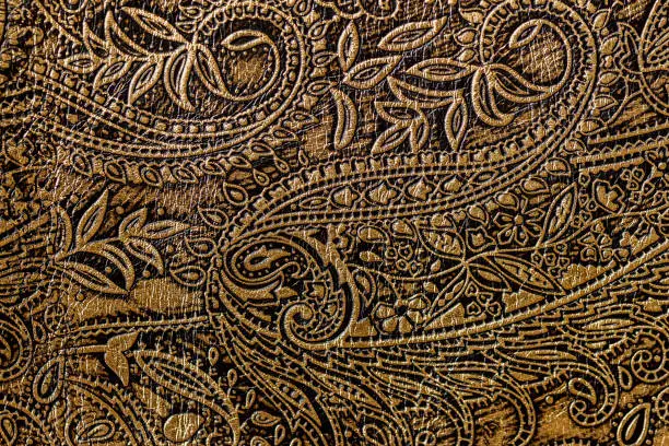 Photo of Texture of golden brown genuine leather close-up, with embossed floral trend pattern, wallpaper or banner design