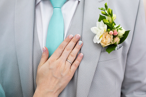 Wedding boutonniere on suit of groom and bride’s hand