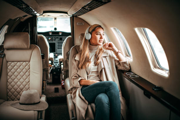 Young fashionable woman sitting on a private airplane and listening to music through headphones Young fashionable woman sitting in a private jet and listening to music through the headphones. She is looking through the window. vehicle interior audio stock pictures, royalty-free photos & images