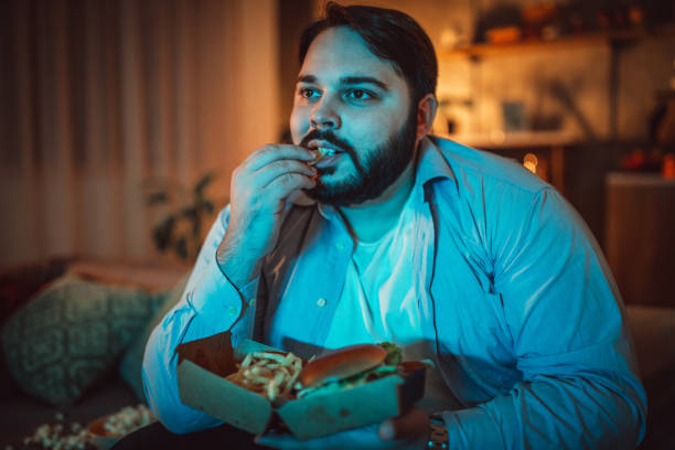 One man, sitting at home, eating burgers and watching a movie alone.