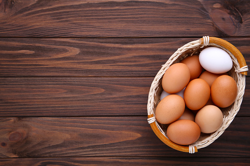 Chicken eggs in basket on brown wooden background