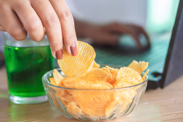 istock woman hand eating fast food potato chips with soda glass while working on computer 1076593474