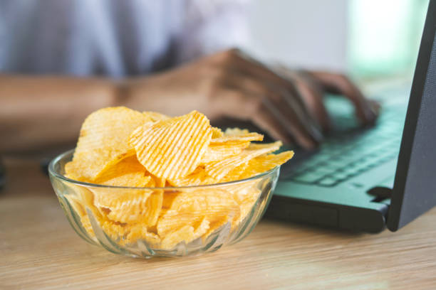 chips de pommes de terre dans un bol sur le bureau avec flou fond de femme qui travaille - computer chip photos et images de collection