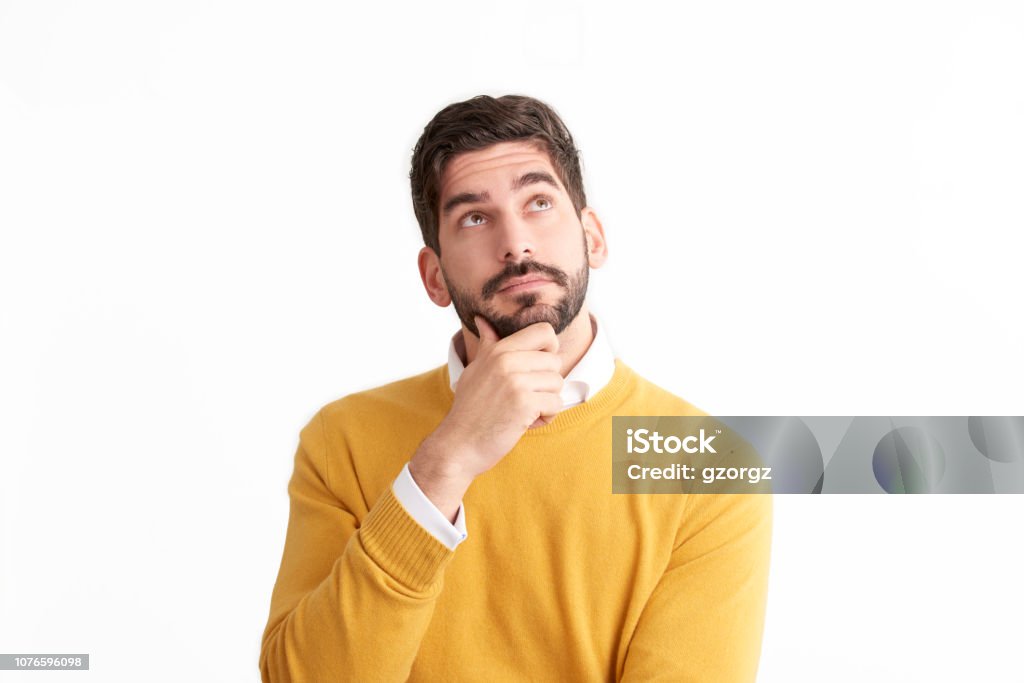 Handsome young man looking thoughtfully at isolated white background with copy space Portrait shot of casual man looking thoughtfully while standing at isolated white background and looking up. Contemplation Stock Photo