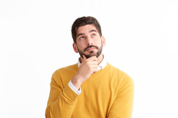 Handsome young man looking thoughtfully at isolated white background with copy space Portrait shot of casual man looking thoughtfully while standing at isolated white background and looking up. looking up stock pictures, royalty-free photos & images