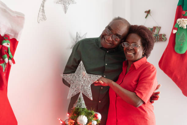 istock Sweet elder black couple embracing each other while smiling at camera standing behind the christmas tree 1076600878