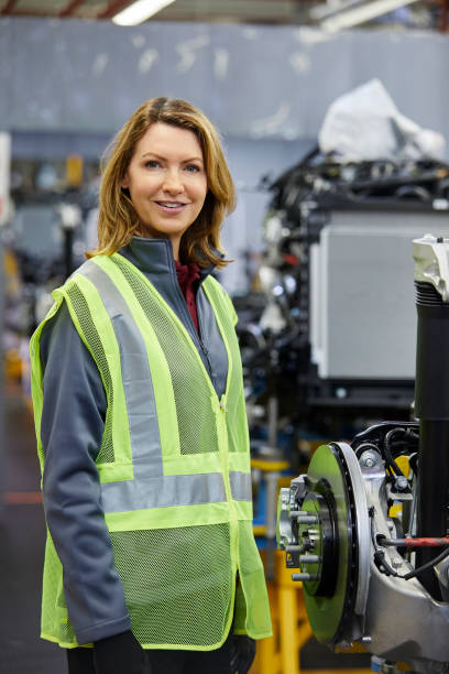 smiling female engineer standing by car part - automobile industry transportation indoors vertical imagens e fotografias de stock