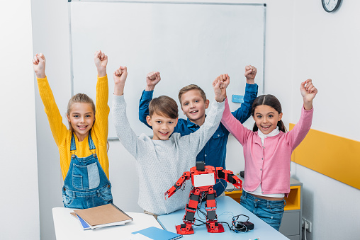 happy schoolchildren raising hands, smiling and looking at camera in stem class