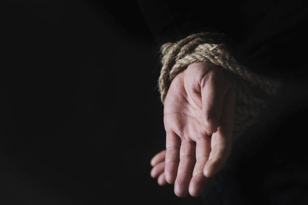 man with his hands tied behind his back closeup of a man with his hands tied behind his back with rope, against a black background with some blank space on the left hostage photos stock pictures, royalty-free photos & images
