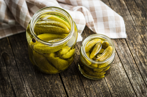 Pickles. Preserved cucumbers in jar on wooden table.