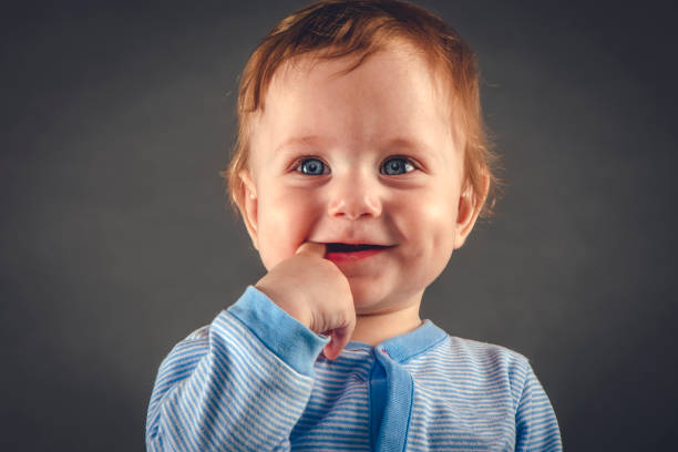 retrato de estudio de niño de 9 meses sobre fondo gris-azul - finger in mouth fotografías e imágenes de stock
