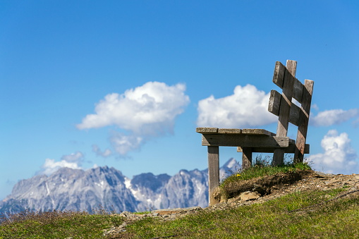 Empty wooden bench with idyllic Alps mountains landscape, low angle view, sunny summer day