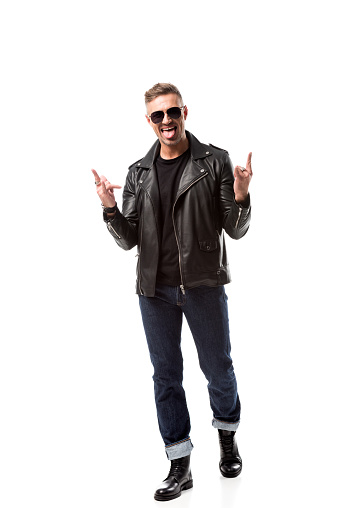 excited stylish man in leather jacket showing rock signs and sticking out tongue isolated on white