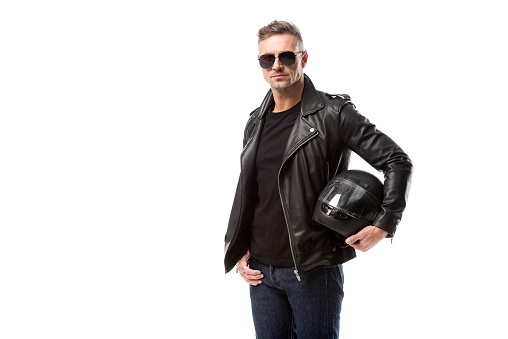 stylish man in leather jacket and sunglasses holding motorcycle helmet isolated on white