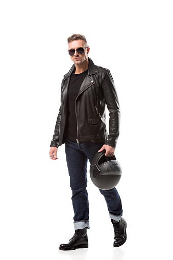 handsome man in leather jacket and sunglasses holding motorcycle helmet isolated on white