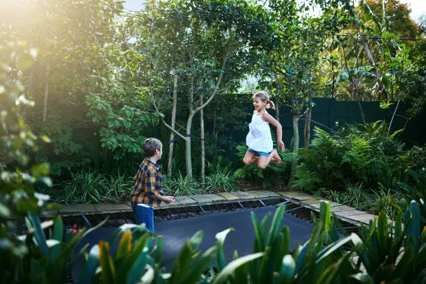 Shot of an adorable little boy and girl jumping on a trampoline in the backyard at home