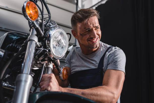 istock smiling mechanic checking motorcycle front wheel in garage 1076666992