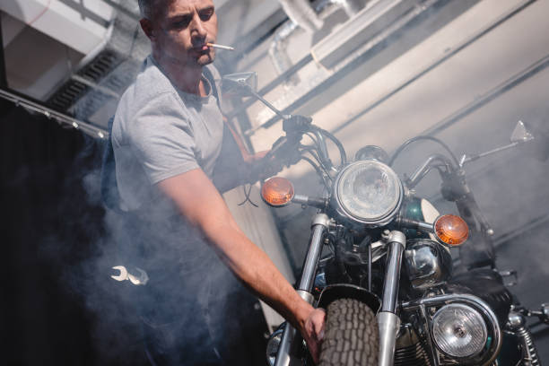 istock guy smoking cigarette and checking motorbike front wheel in garage 1076667240