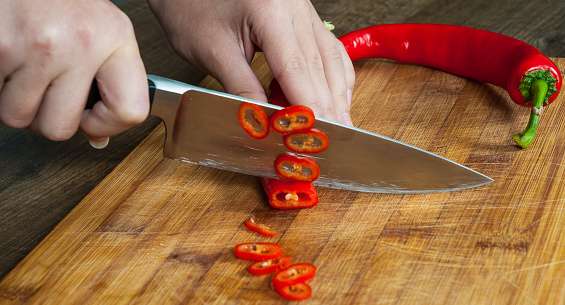 Chefs hands chopping chili pepper on wooden board