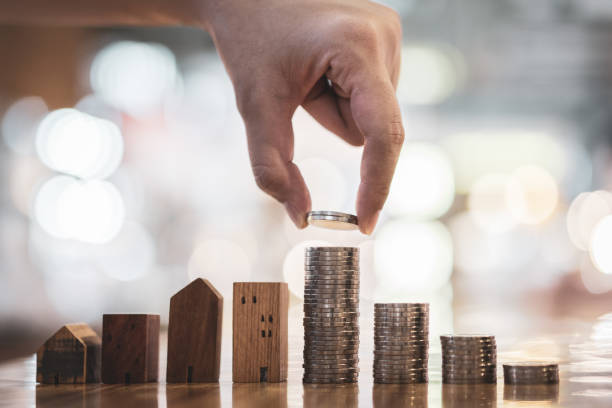 Hand choosing row of coin money on wood table and mini wood house, selective focus, Planning to buy property. Choose what's the best. A symbol for construction ,ecology, loan concepts stock photo